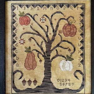 May include: Framed cross-stitch sampler featuring a tree with pumpkins and acorns. The tree is brown with pumpkins in shades of orange and white. The sampler includes the alphabet and numbers, with the text "Three Sheep Studio.com" at the bottom.
