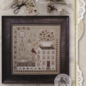 May include: A framed cross-stitch sampler titled "Winter Rose Manor" by Brenda Gervais. The sampler features a detailed house, birds, and floral elements in shades of brown, red, and green. The text "Sampler & Pincushion" is visible.