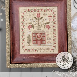 May include: Framed cross-stitch sampler with a red house, flowers, and the text "ABC ~ 123 SAMPLER." The sampler is in a gold and red frame. The design includes a bird and floral elements.