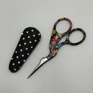 May include: Floral pattern embroidery scissors with a black and white polka dot case. The scissors have a colorful floral design on the handles and a silver blade. The case is black with white polka dots.