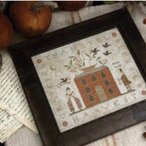 May include: A framed cross-stitch design with a brown wooden frame. The design features a house with a red roof and a tree with birds. The text "Grateful, Thankful & Blessed" is stitched in the upper left corner and "The Harvest" is stitched in the lower right corner.