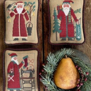 May include: Four embroidered pillow covers featuring different scenes of Santa Claus. The pillows are beige with red, green, and white accents. The scenes include Santa with a bird, Santa with a sack of gifts, Santa with a sewing machine, and Santa with a bucket.