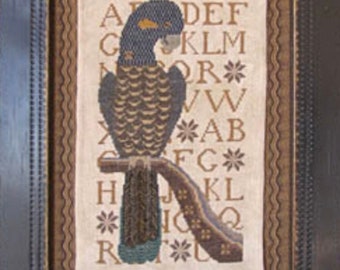 May include: Framed cross-stitch artwork featuring a detailed bird perched on a branch. The bird has blue, brown, and green tones. The background includes an alphabet and floral accents. The frame is dark brown.