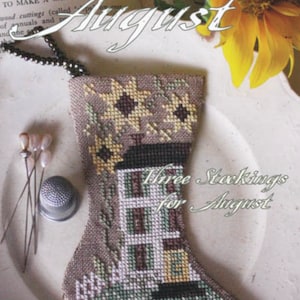 May include: A cross-stitch pattern for a stocking with a house and sunflowers. The pattern is titled "Three Stockings for August" and is by Blackbird Designs.