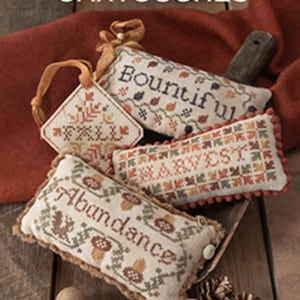 May include: An assortment of autumn-themed needlepoint designs. The image features four embroidered pieces with the words "Fall", "Bountiful", "Harvest", and "Abundance". The designs are in warm colors, with a wooden background and the text "Autumn Cartouches".