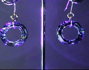 Peut inclure: Une paire de boucles d'oreilles irisées avec un design circulaire. Les boucles d'oreilles sont composées de plusieurs couches de métal qui créent un motif tourbillonnant. Les boucles d'oreilles sont d'une couleur violet foncé avec des reflets bleus et verts.