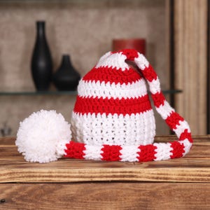 Op de afbeelding: Een rood-wit gestreepte gebreide muts met een witte pompon aan het einde van een lange staart.