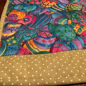 Puede incluir: Un camino de mesa verde con lunares blancos. El camino de mesa tiene un borde colorido con un patr&oacute;n de huevos de Pascua.