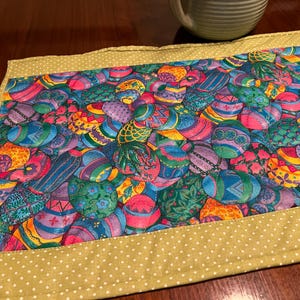 Puede incluir: Un camino de mesa verde con lunares blancos presenta un patr&oacute;n colorido de huevos de Pascua. Los huevos est&aacute;n decorados con varios dise&ntilde;os y colores, incluyendo morado, azul, verde, amarillo y rosa.