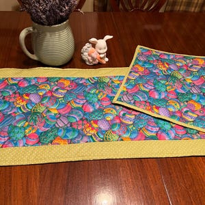 Puede incluir: Dos caminos de mesa coloridos con un patr&oacute;n de huevos de Pascua. Los caminos de mesa son verdes, azules, morados y amarillos. Los caminos de mesa tienen un borde amarillo con lunares blancos.