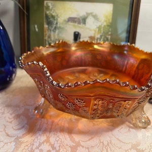 May include: A vintage amber glass bowl with a scalloped edge and three feet. The bowl features a butterfly and grape design.