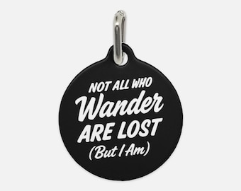 May include: Black round dog tag with a silver ring. The tag has white text that reads "Not all who wander are lost (But I am)"