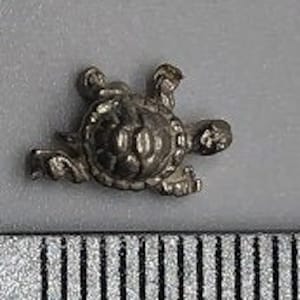 May include: A small silver turtle charm, approximately 1 cm in length. The turtle is in a walking position with its head and legs extended.
