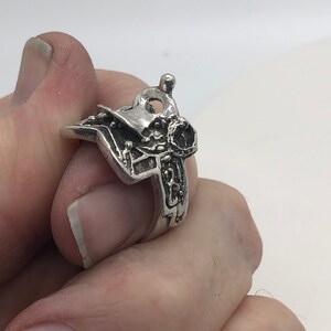 May include: A silver ring featuring an intricate design of a saddle and stirrups.