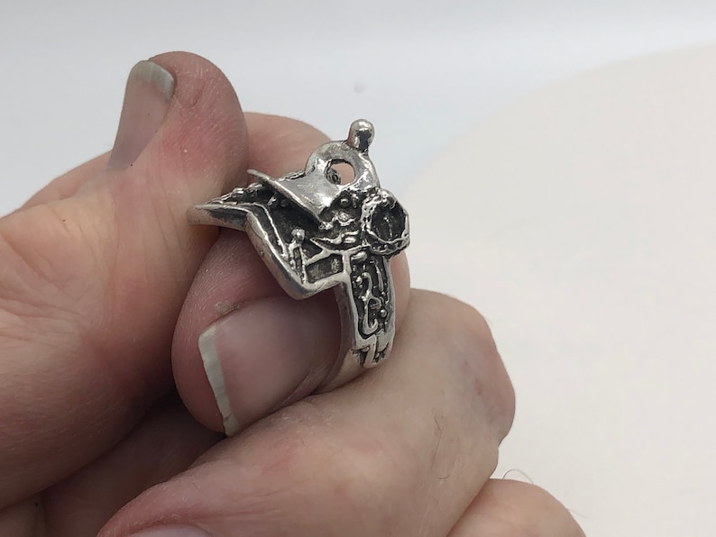 May include: A silver ring featuring an intricate design of a saddle and stirrups.