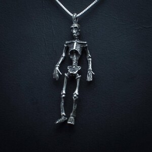 May include: A silver skeleton pendant necklace. The skeleton is detailed and has a realistic look. The necklace is on a silver chain.