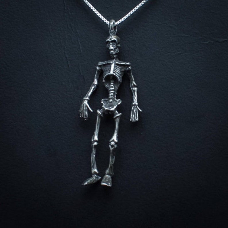May include: A silver skeleton pendant necklace. The skeleton is detailed and has a realistic look. The necklace is on a silver chain.