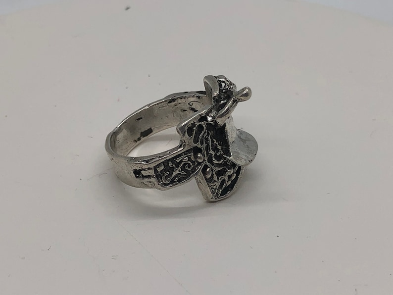 May include: A silver ring featuring a detailed saddle design. The ring is made of metal and has a polished finish.