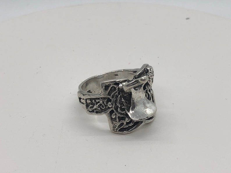 May include: A silver ring featuring an intricate design of a saddle. The ring is crafted from metal and has a polished finish.