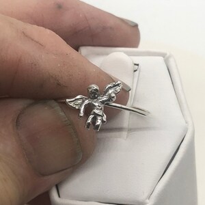 May include: A silver ring with a cherub design. The cherub is holding a heart in its hands.