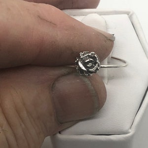 May include: A silver ring with a rose design. The ring is on a white background.