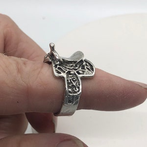 May include: A silver ring shaped like a saddle with intricate details.