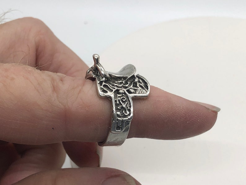 May include: A silver ring shaped like a saddle with intricate details.