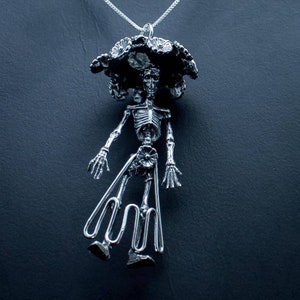 May include: Silver pendant necklace featuring a skeletal figure wearing a flower crown. The figure is depicted in a standing pose with its arms outstretched.