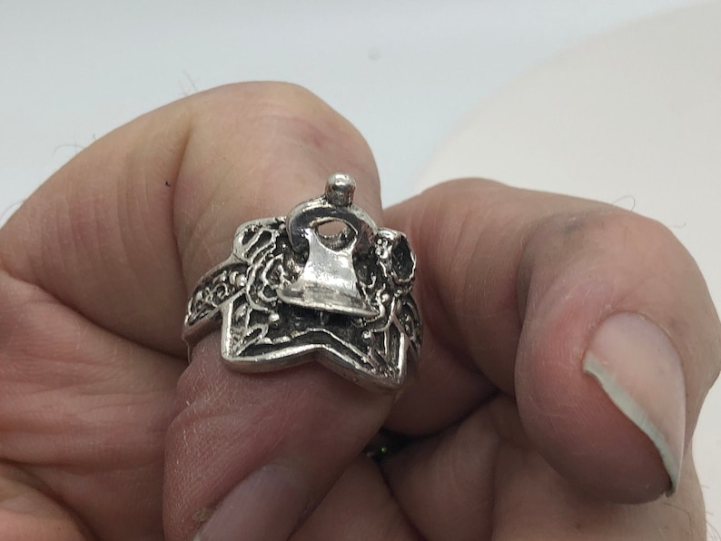 May include: A silver ring with a detailed design featuring a star shape and a small, raised, circular element on top.