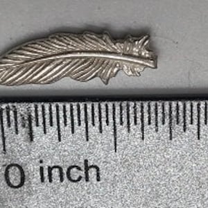 May include: A silver feather charm pendant, approximately 1 inch long, with detailed feather markings.