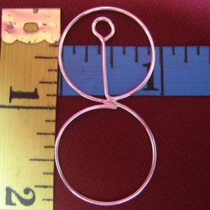 May include: Two silver hoops connected by a vertical bar, the top hoop is slightly larger than the bottom hoop. The hoops are shown against a red background with a blue measuring tape.