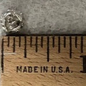May include: A small silver charm in the shape of a wreath with a small bird inside. The charm is about 1/2 inch in diameter.