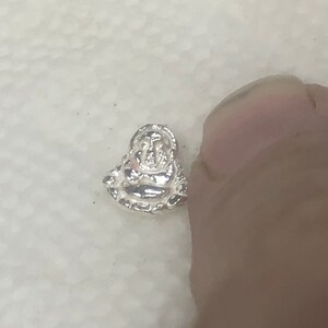 May include: A silver charm featuring a detailed depiction of a seated Buddha.