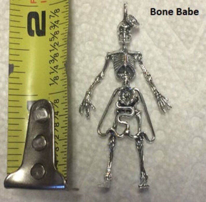 May include: Silver skeleton charm with a detailed anatomical design, including internal organs. The charm is approximately 2 inches tall and features the text "Bone Babe".