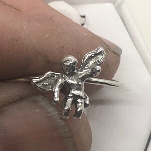 May include: A silver ring with a small angel charm. The angel is depicted with wings outstretched and a halo.