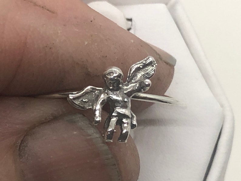 May include: A silver ring with a small angel charm. The angel is depicted with wings outstretched and a halo.