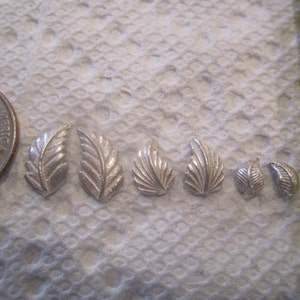 May include: Seven silver leaf charms of varying sizes. The charms are in the shape of a leaf with a detailed design.