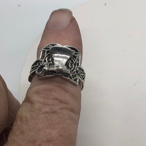 May include: A silver ring with a detailed design featuring a raised, ornate, bell-shaped centre piece.