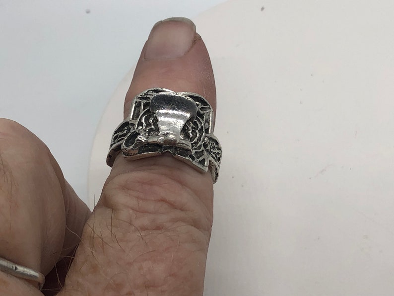 May include: A silver ring with a detailed design featuring a raised, ornate, bell-shaped centre piece.