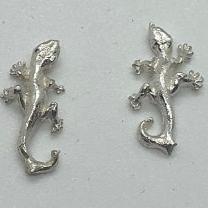 May include: A pair of silver gecko earrings. The geckos are facing to the right and have detailed features.