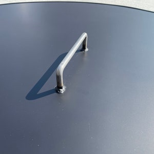 May include: A black metal lid with a silver handle. The lid is round and has a smooth surface.