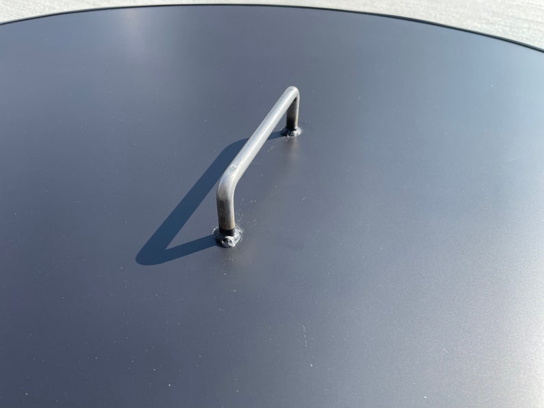 May include: A black metal lid with a silver handle. The lid is round and has a smooth surface.