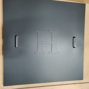 May include: A dark gray door with a large, white, embossed letter "H" in the center. The door has two silver handles on either side.