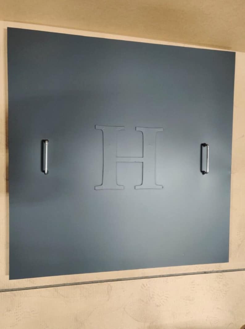 May include: A dark gray door with a large, white, embossed letter "H" in the center. The door has two silver handles on either side.