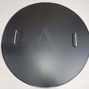 May include: Black round metal cover with two silver handles and the letter "A" embossed in the center.