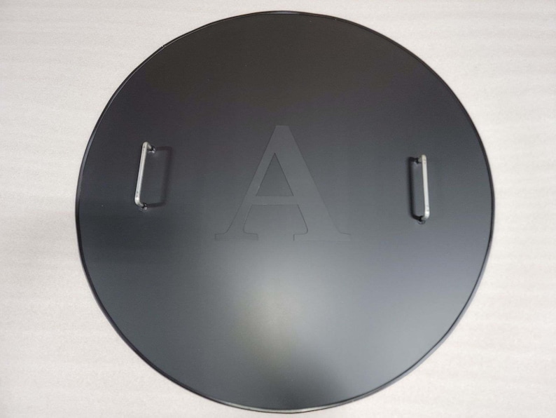 May include: Black round metal cover with two silver handles and the letter "A" embossed in the center.