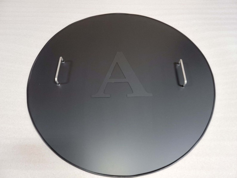 May include: Black round metal fire pit lid with two handles and the letter "A" engraved in the center.