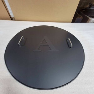 May include: Black round metal fire pit lid with two handles and a logo of a stylized letter A.