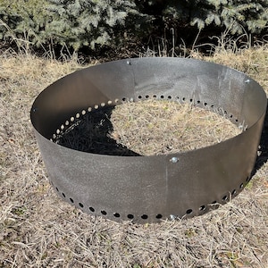May include: A round, metal fire pit ring with holes around the edge. The ring is sitting on a bed of dry grass.