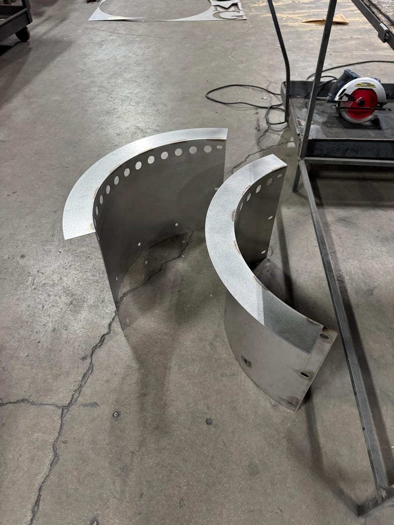 May include: Two curved, semi-circular metal panels made of brushed stainless steel. Each panel features a flat, horizontal top flange with a series of evenly spaced circular perforations along the edge and additional mounting holes on the vertical sides.